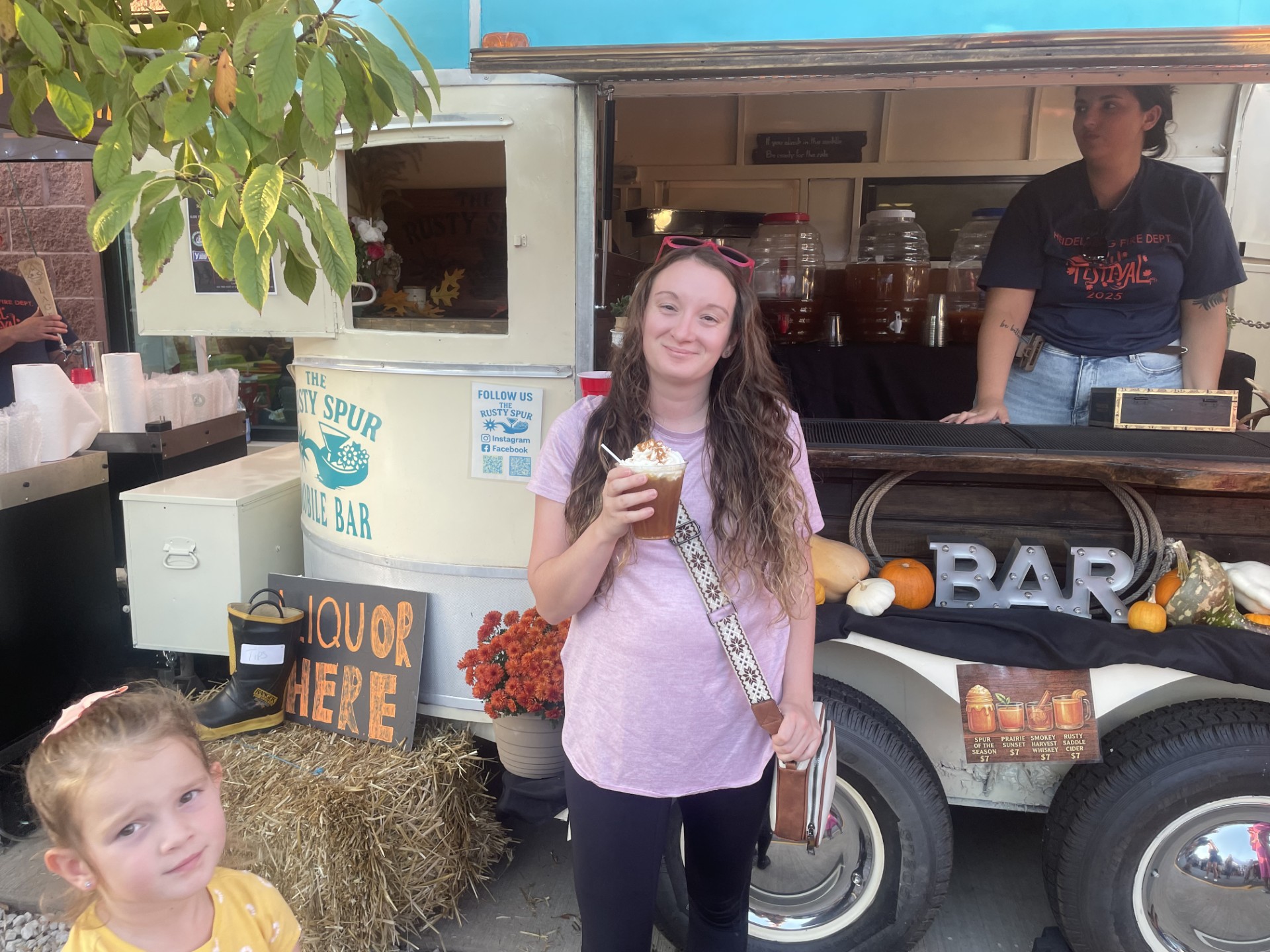 A guest showing off her whipped-cream-topped cider in front of the trailer at a fall festival
