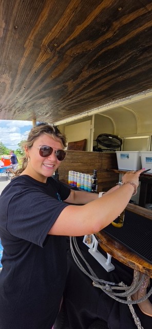 Hannah serving drinks from inside The Rusty Spur trailer bar under the rustic wood awning