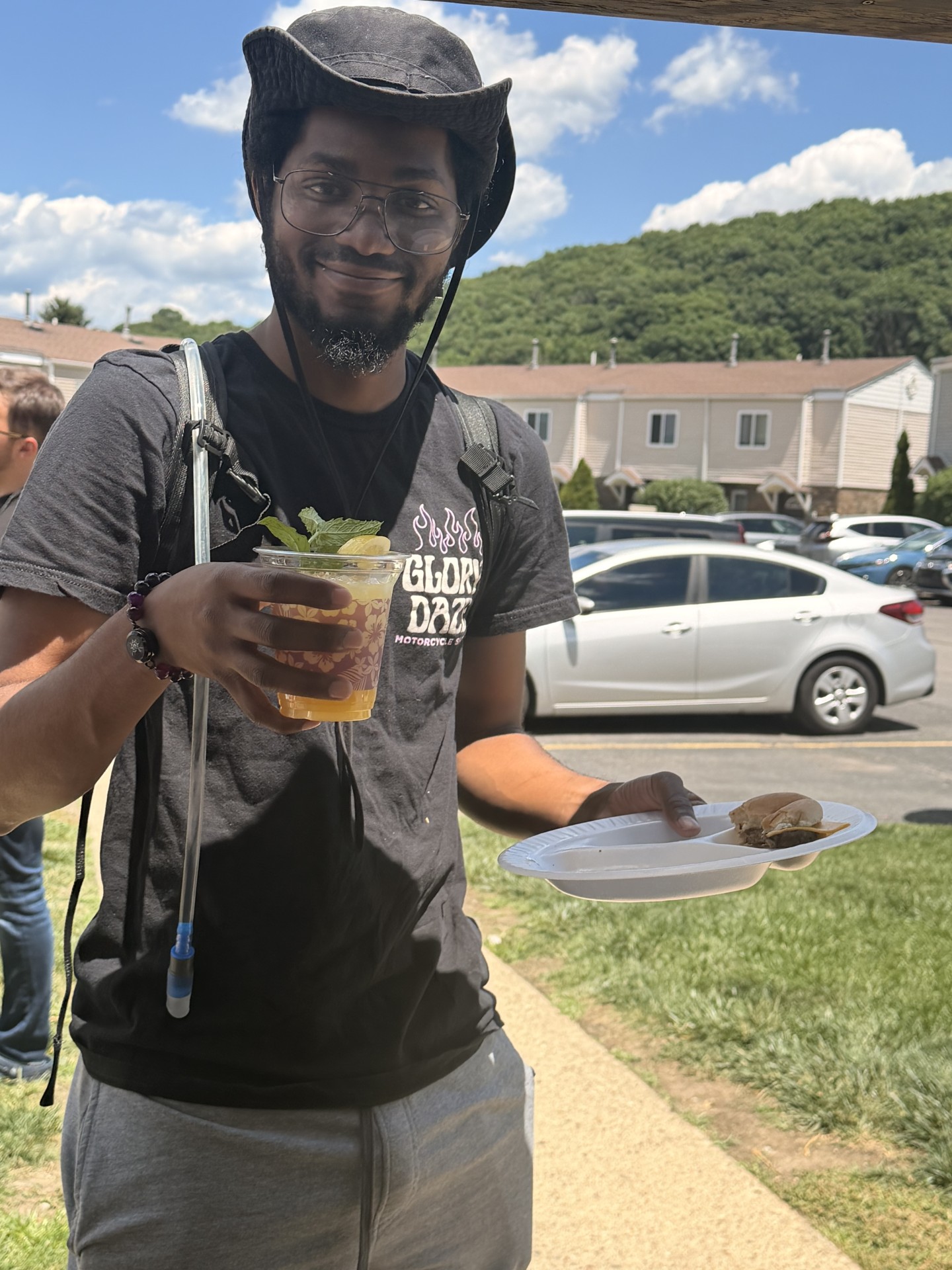 A guest in a cowboy hat holding a mint-garnished cocktail at a sunny outdoor event