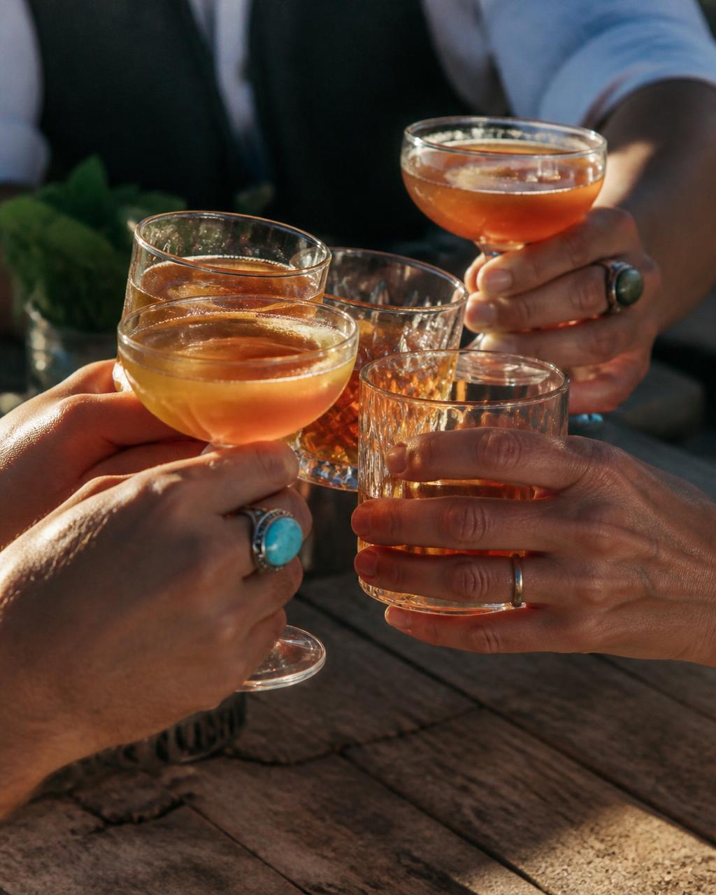 Hands clinking coupe and old fashioned glasses over the trailer's wooden bar top